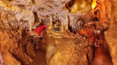 Interior of a cave with stalactites and stalagmites, dimly lit with yellow-orange lights.