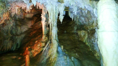Underground cave with stalactites and stalagmites, partially lit.