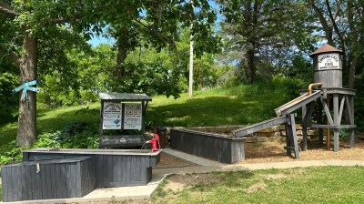 Outdoor mining exhibit with wooden structures and trees in a park setting.