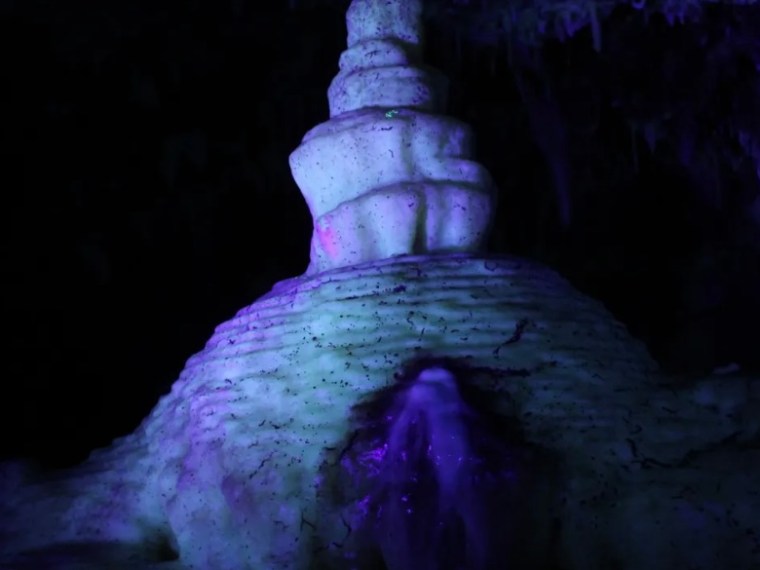 Purple-lit stalagmite formation in a dark cave.