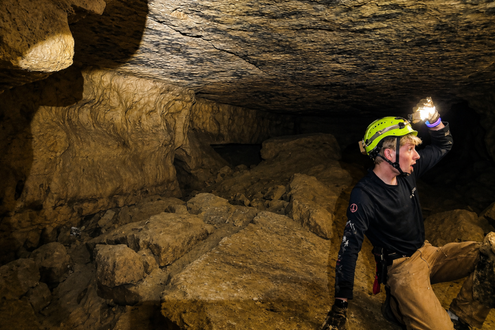 Person in helmet exploring rocky cave with flashlight.