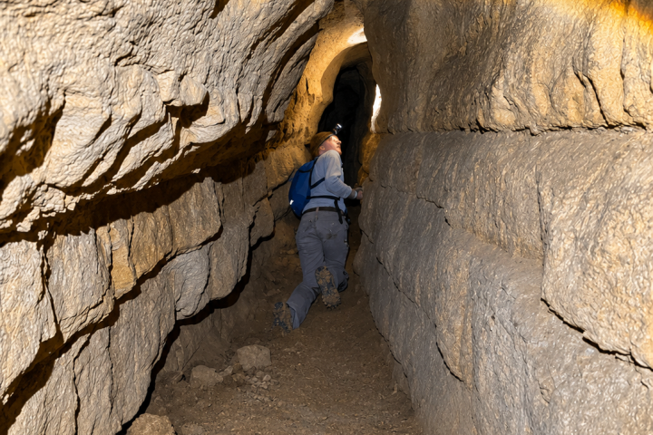 Person walking through narrow, rocky tunnel with a backpack.