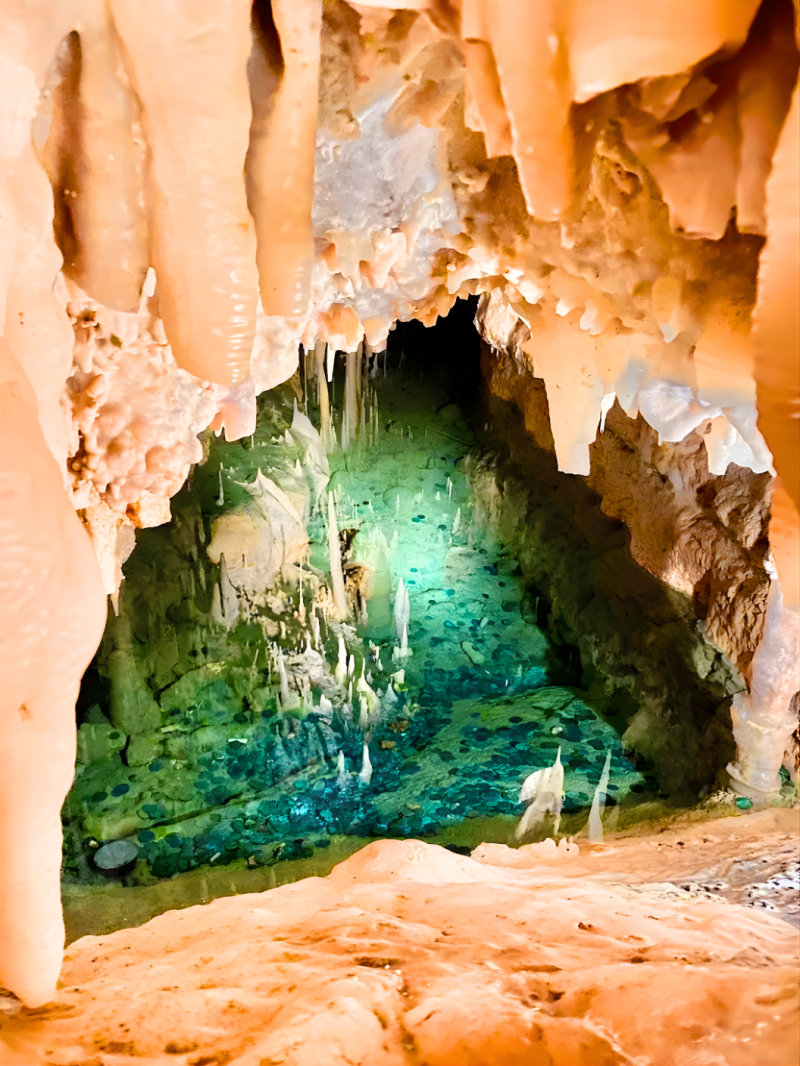 Cave with stalactites and a turquoise water pool.