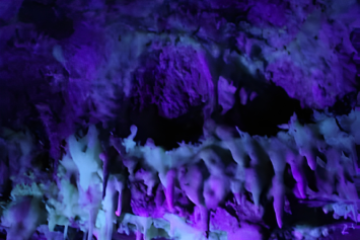 Cave with stalactites illuminated by purple light.