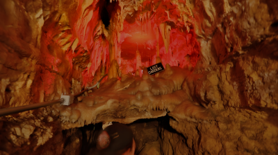 Colorful cave interior with stalactites and a warning sign.