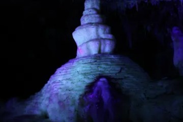 Stalagmite illuminated with purple and blue lights in a dark cave.