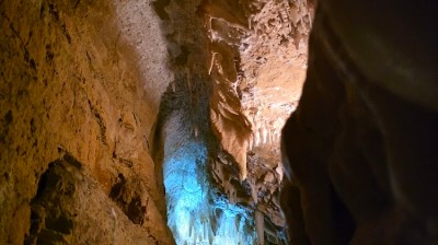 Person in cave with stalactites, illuminated by blue light.