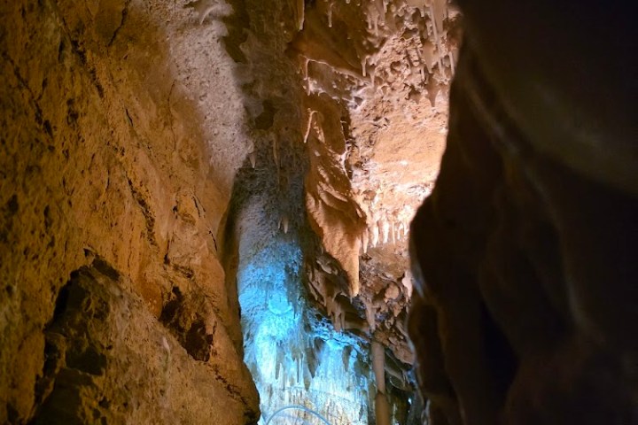 Person in cave with stalactites, illuminated by blue light.