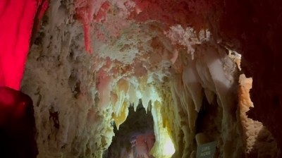 People exploring a narrow, dimly lit cave with red and white rock formations.