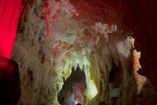 People exploring a narrow, dimly lit cave with red and white rock formations.