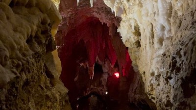 Narrow cave passage with stalactites and dim, red lighting.