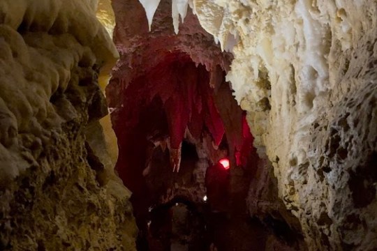 Narrow cave passage with stalactites and dim, red lighting.