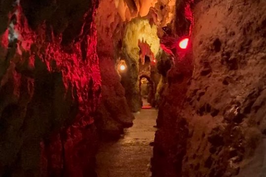 Narrow cave passage with red lighting and rock formations.