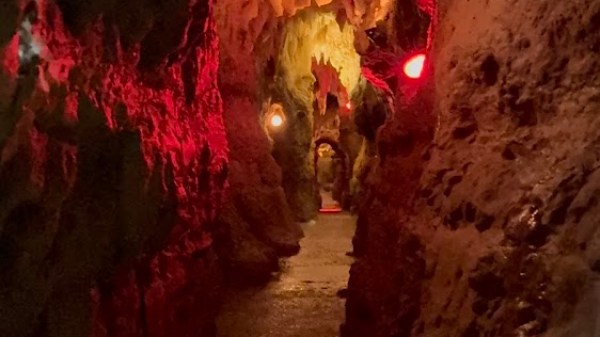 Narrow cave passage with red lighting and rock formations.