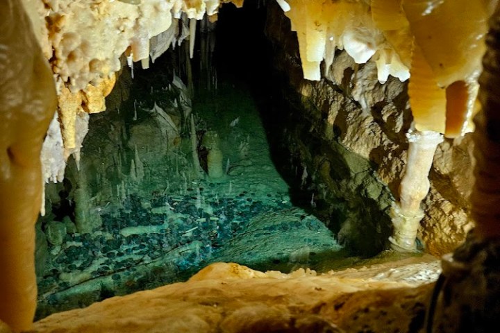 Cave interior with stalactites and a shallow pool of water.