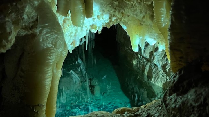Cave with stalactites and turquoise water pool.