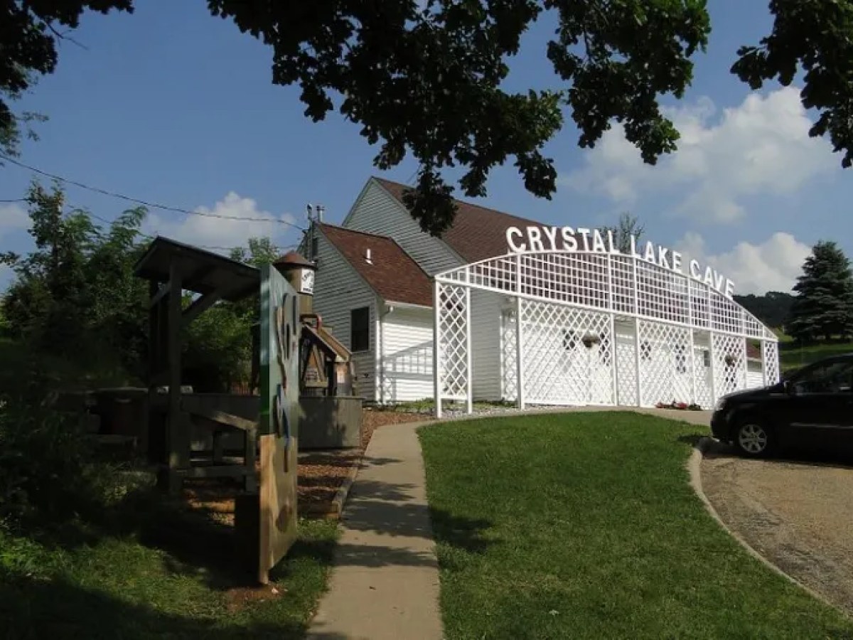 White building with lattice labeled 'CRYSTAL LAKE CAVE' under a cloudy blue sky.