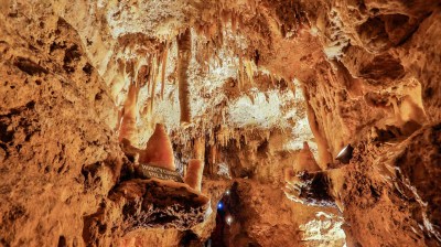 Cave interior with stalactites and stalagmites, illuminated by warm lights.
