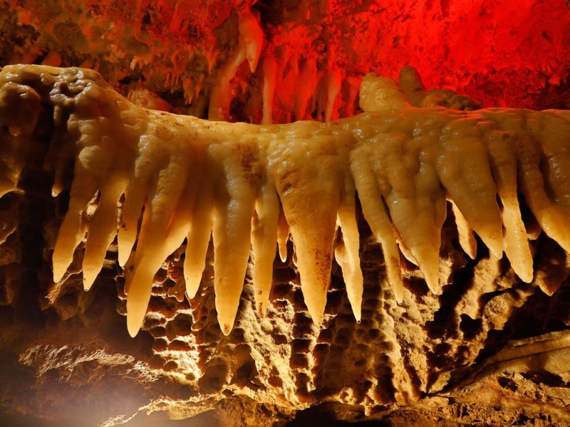 Stalagmites and stalactites in cave with orange-red lighting.