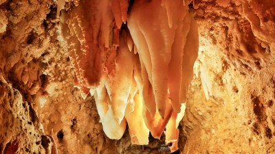 Person exploring cave with large stalactites hanging from ceiling.