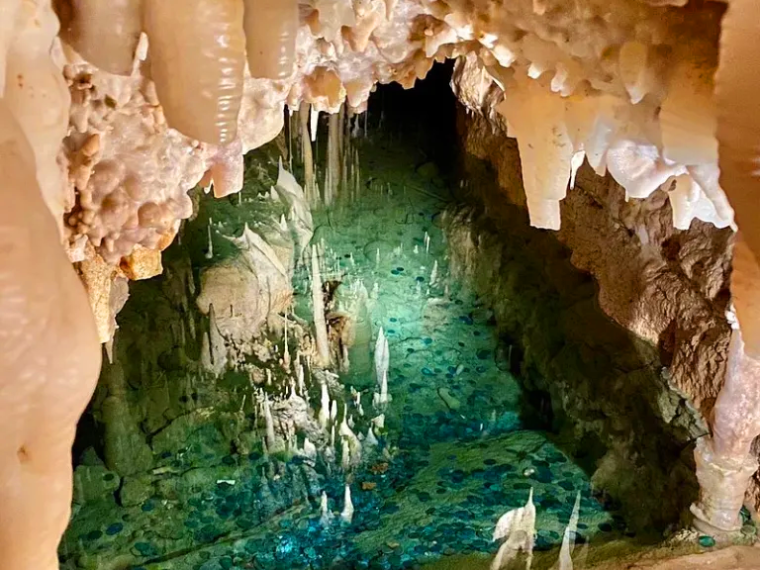 Cave interior with stalactites and a turquoise pool.